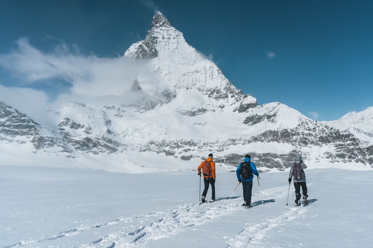Three hikers trek across snowfields with Matterhorn peak in view, Zermatt, Switzerland.